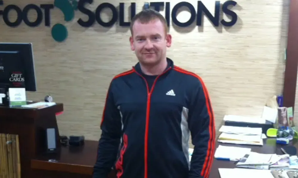 A man is standing in front of a sign that says foot solutions