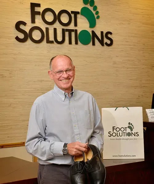 A man holding a pair of shoes in front of a foot solutions sign