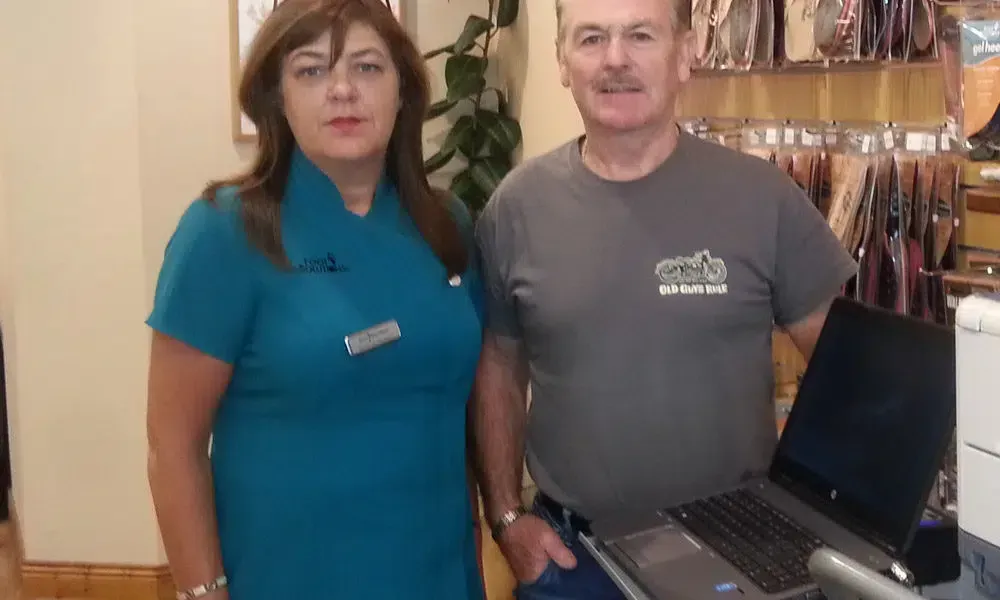 A man and a woman are standing next to each other in front of a laptop.