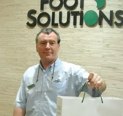 A man is holding a shopping bag in front of a sign that says foot solutions.
