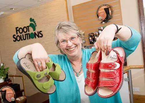 A woman is holding two pairs of shoes in front of a sign that says foot solutions.