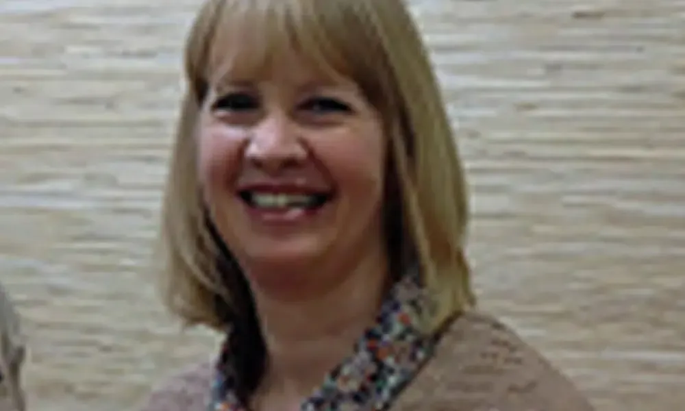 A woman with blonde hair is smiling in front of a brick wall.