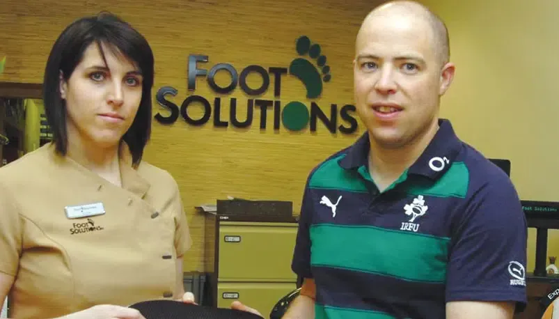 Peter Fitzgibbon and a woman are standing in front of a sign that says foot solutions