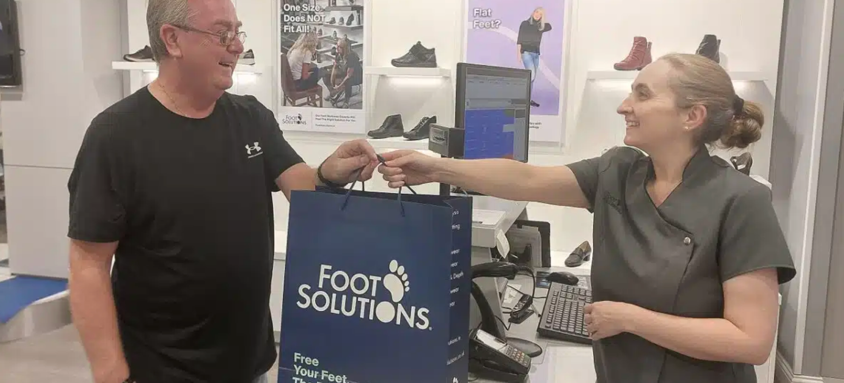 A woman is handing a man a bag in a shoe store.