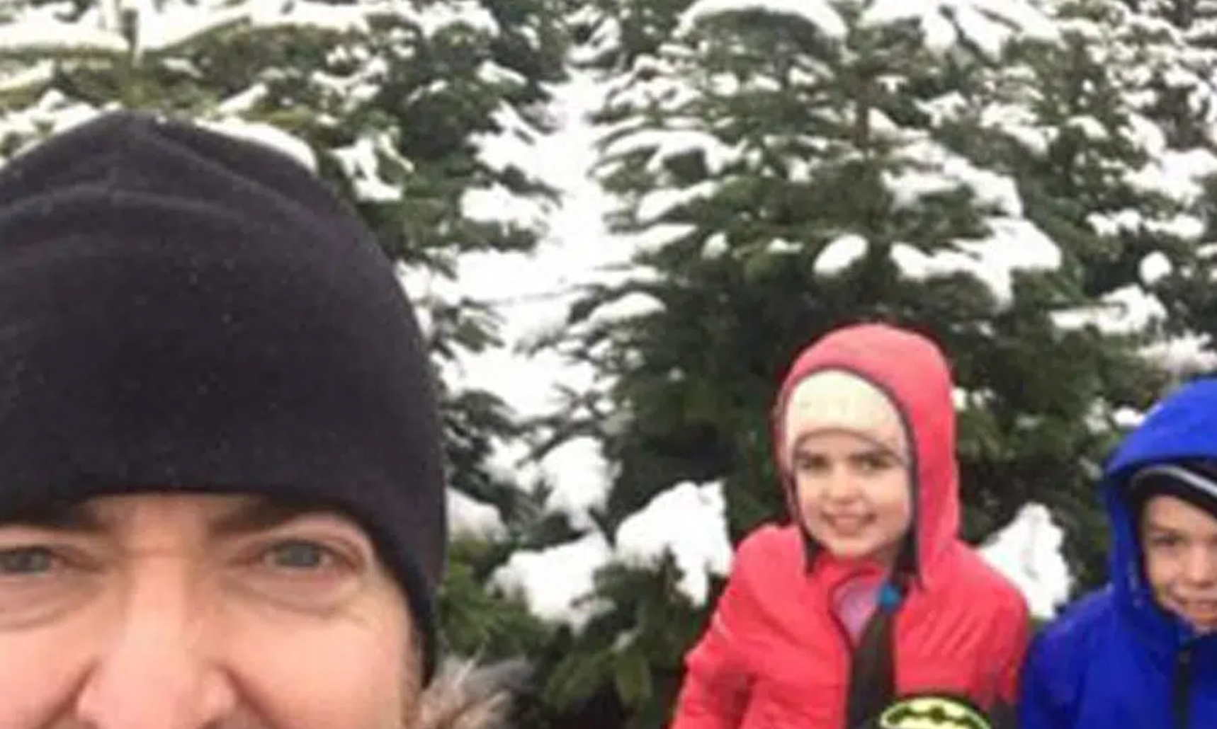 A man and two children are standing in front of a snow covered tree.
