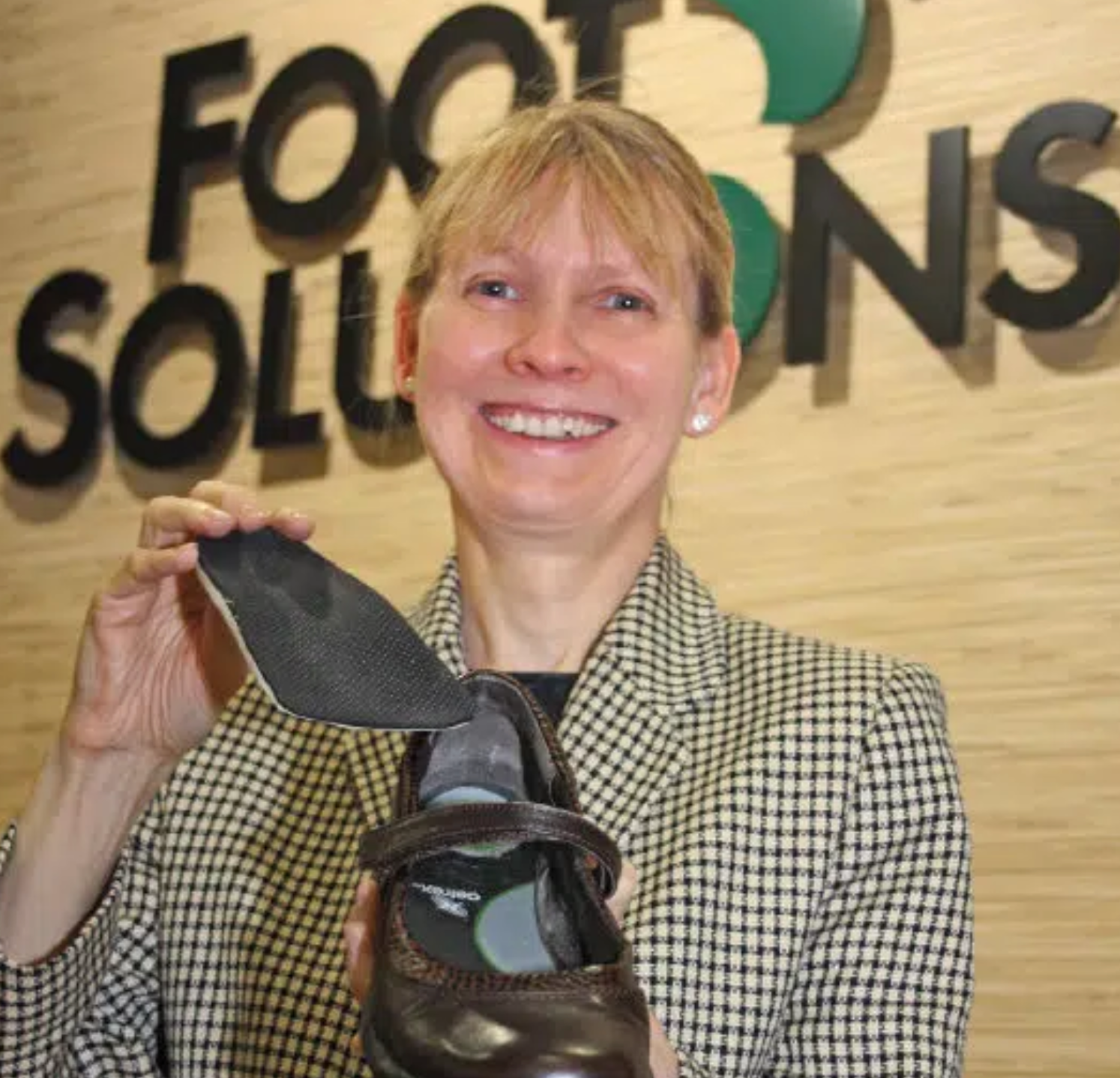 A woman is holding a shoe in front of a sign that says foot solutions