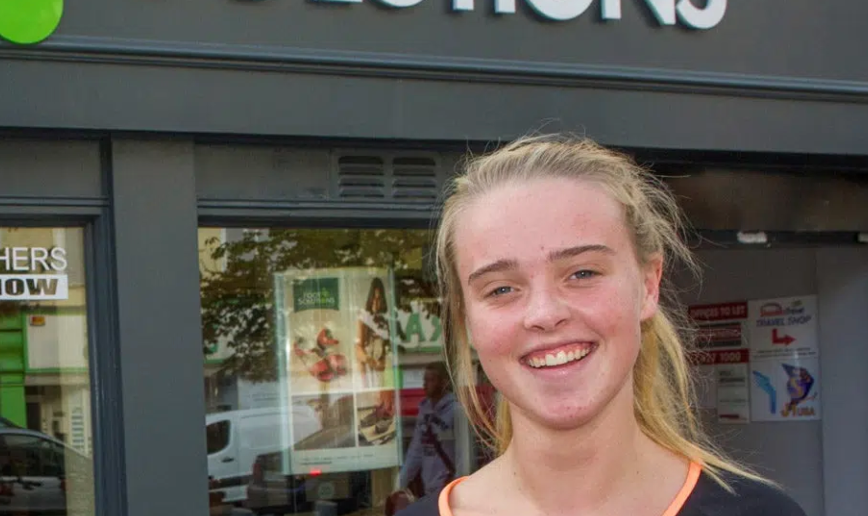 A young woman is smiling in front of a store.