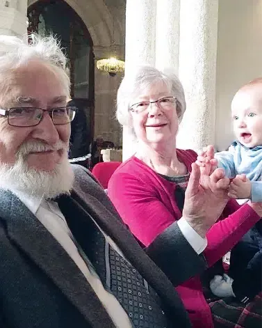 A man with glasses and a beard is sitting next to a woman holding a baby.