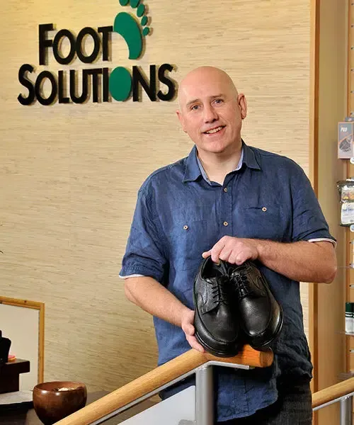 A man holding a pair of shoes in front of a sign that says foot solutions