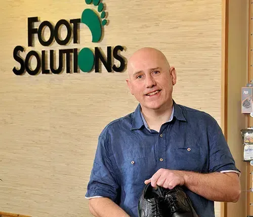 A man is holding a pair of shoes in front of a sign that says foot solutions.
