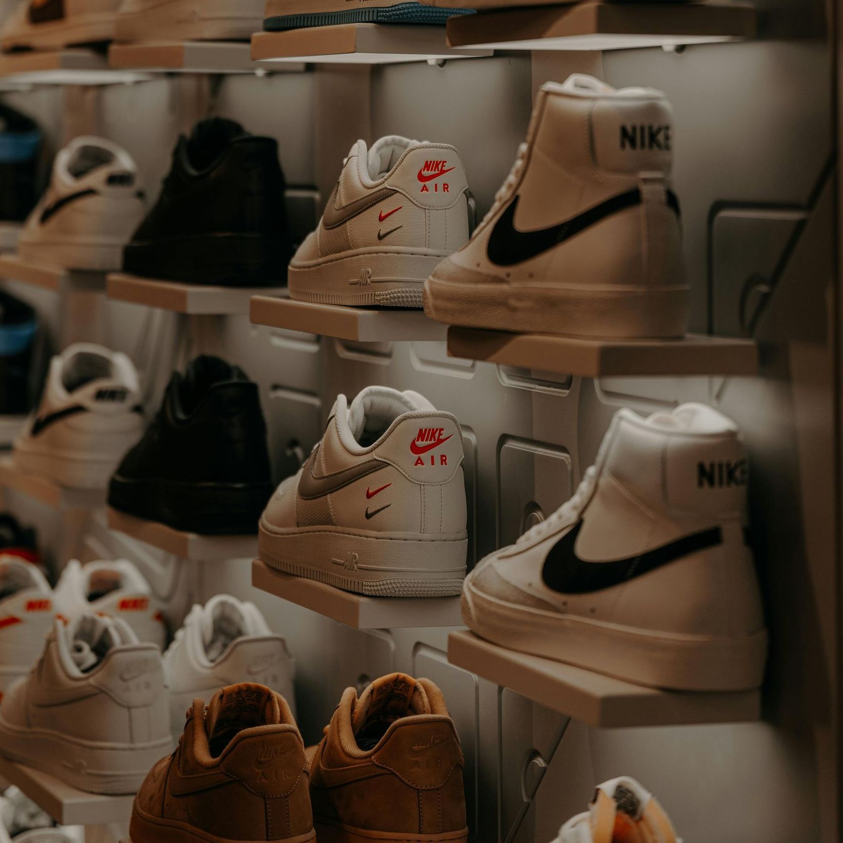 Shelves in a store displaying various Nike sneakers, including white mid-tops and tan low-tops.