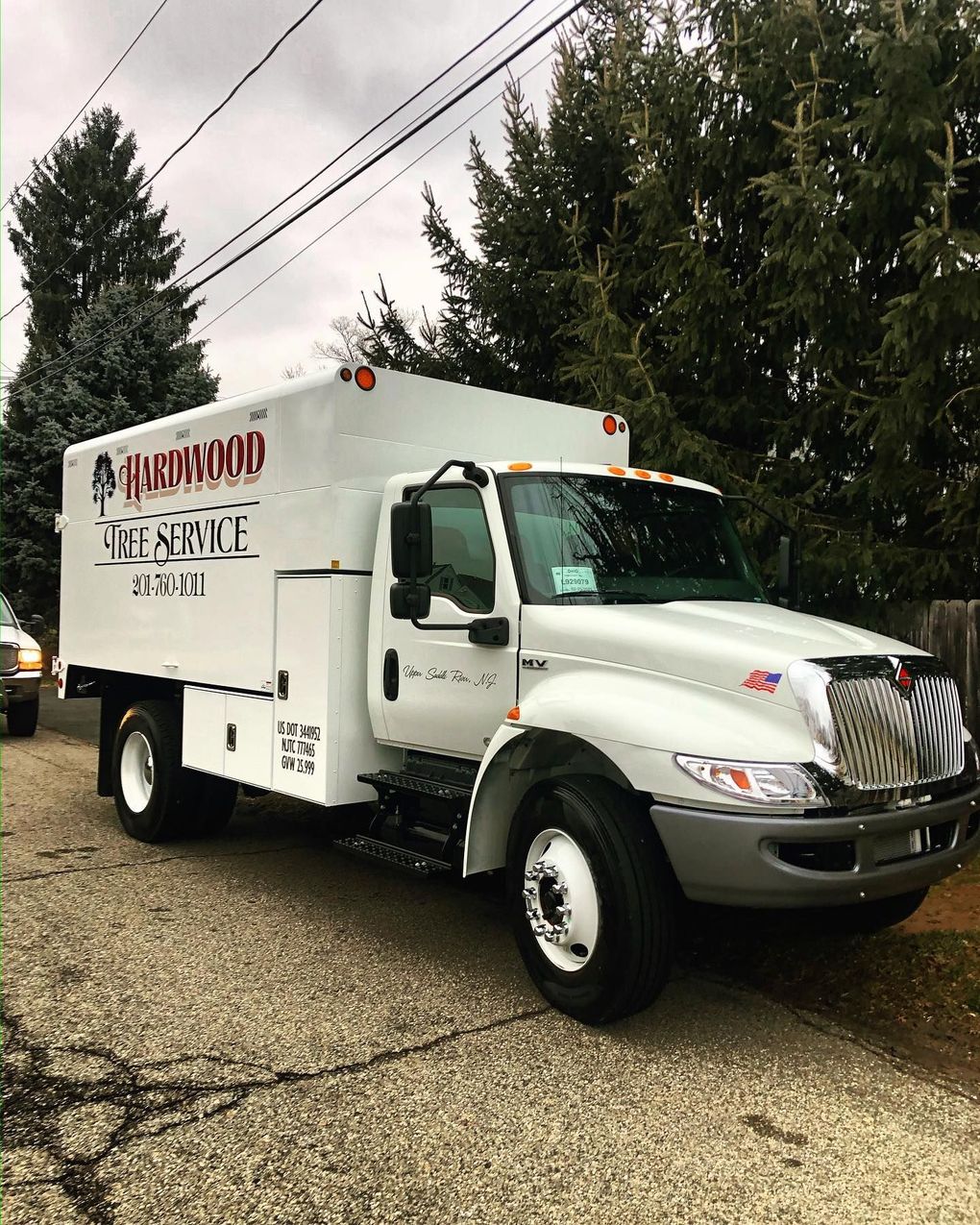 White box truck parked on gravel road under power lines, with trees in the background.