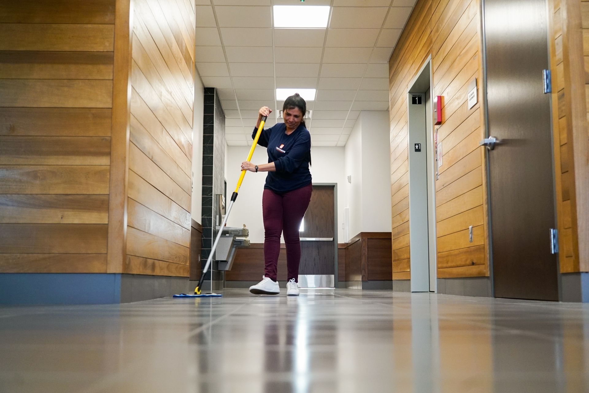 A woman is cleaning the floor of a hallway with a mop.