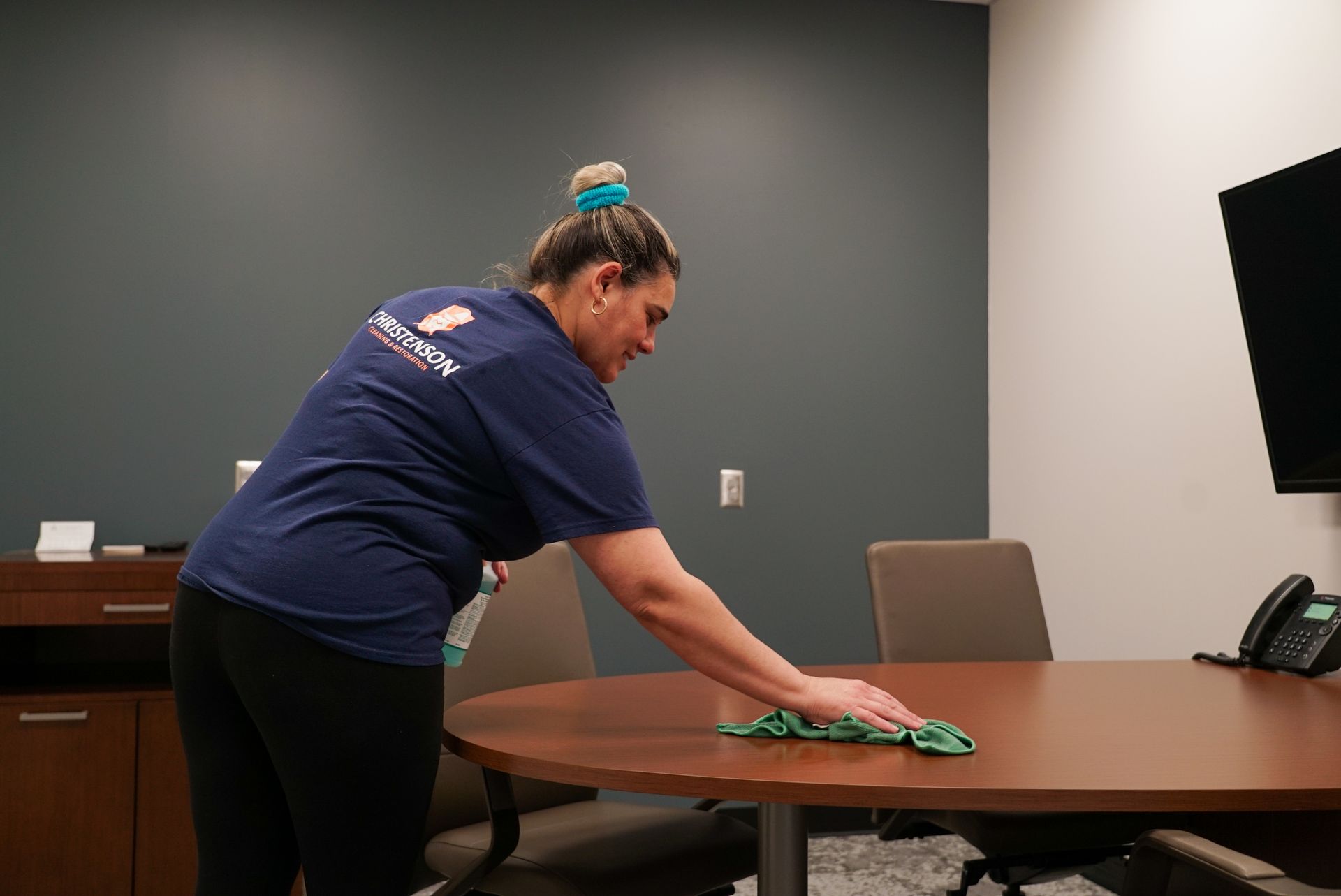 A woman is cleaning a conference room table with a cloth.