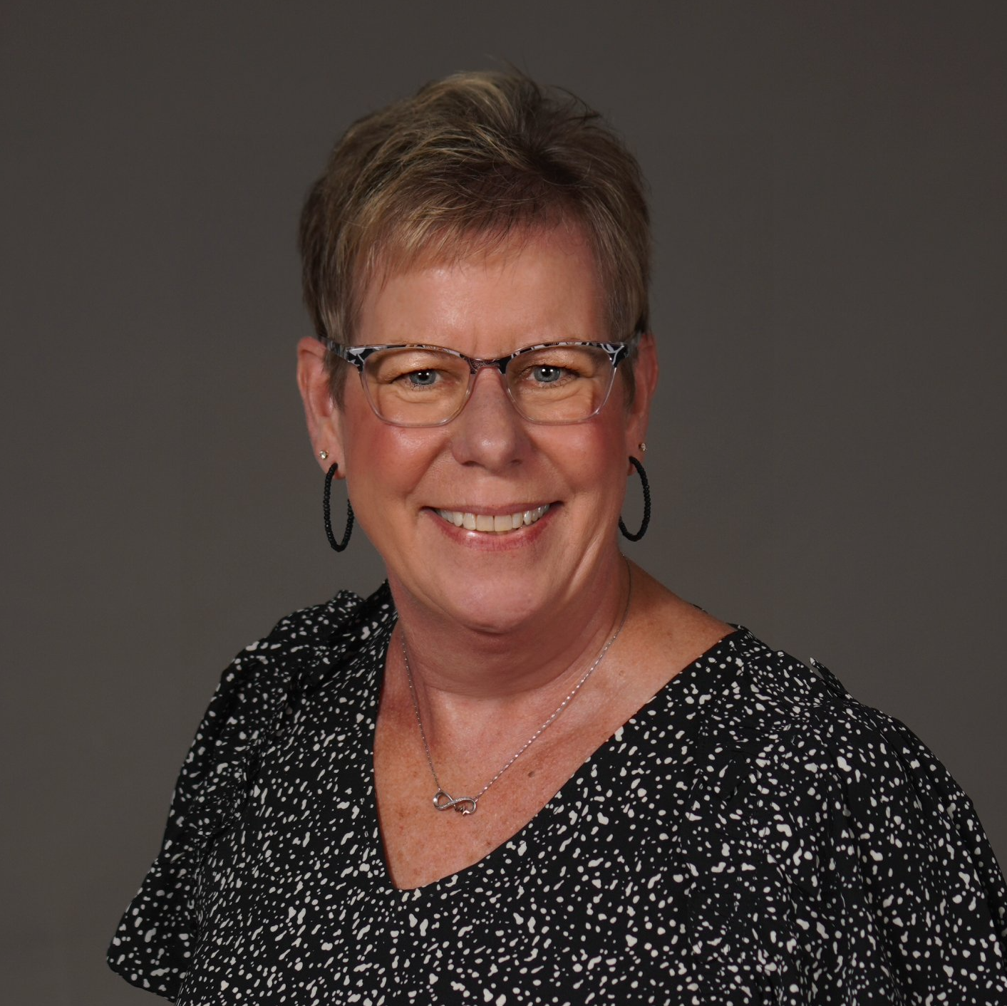 A woman wearing glasses and earrings is smiling for the camera.
