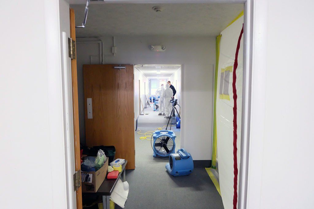 A hallway with a door that is open and a person standing in the background.