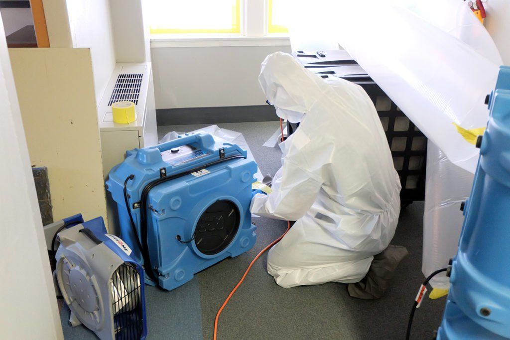 A man in a protective suit is kneeling on the floor in a room.