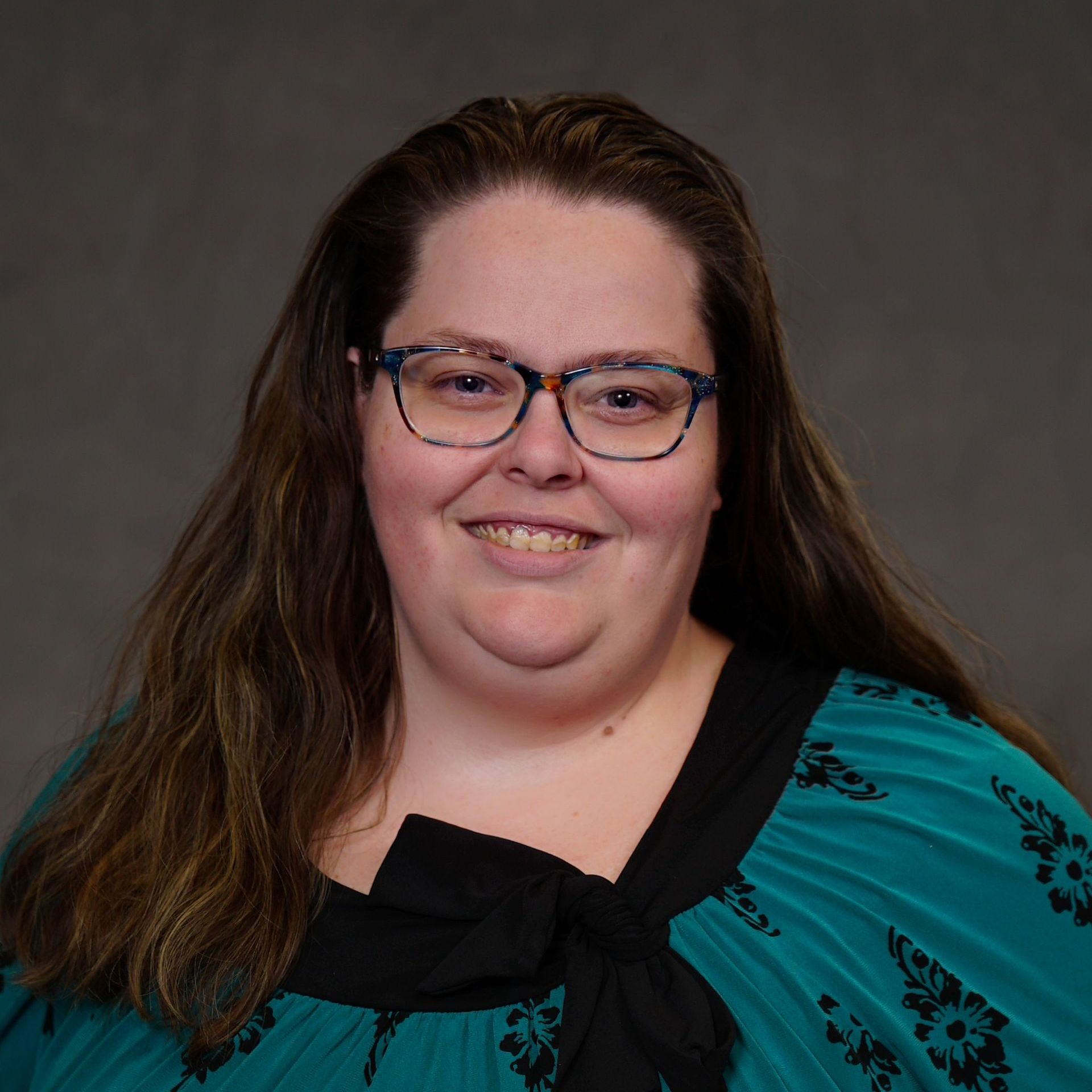 A woman wearing glasses and a green shirt is smiling for the camera.