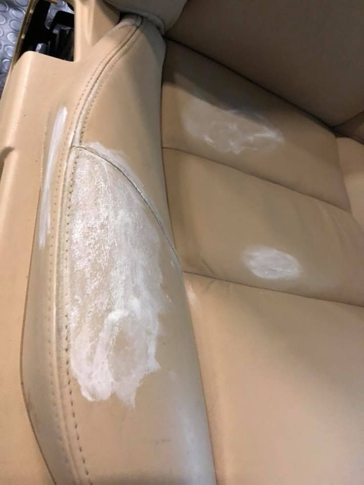 Primo piano di un sedile per auto in pelle marrone chiaro con macchie bianche.