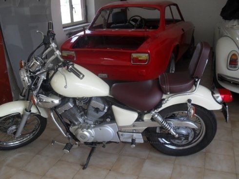 Una motocicletta bianca è parcheggiata accanto a un'auto rossa
