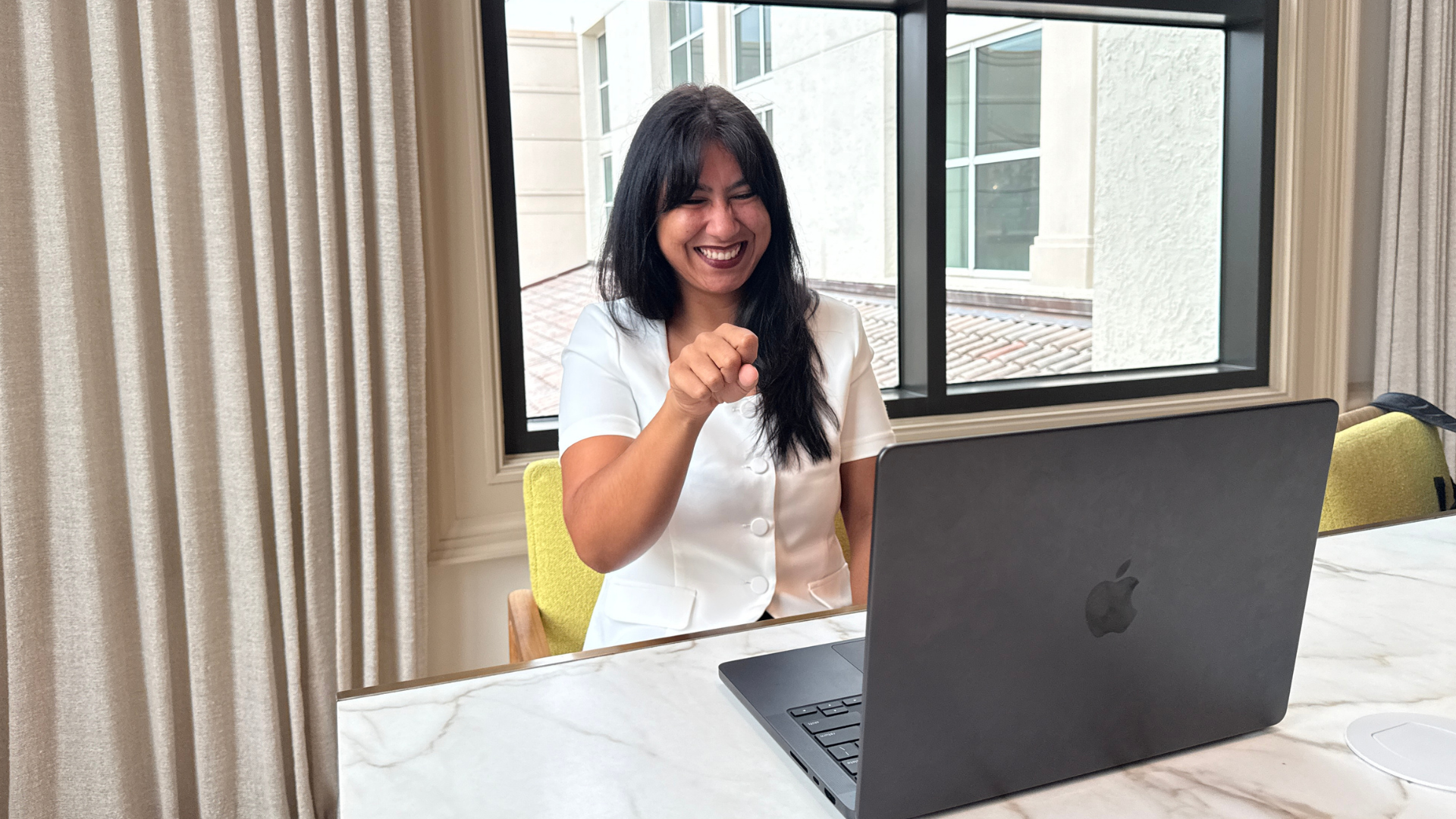 A woman wearing a white shirt signing YES to a laptop with a big smile on.