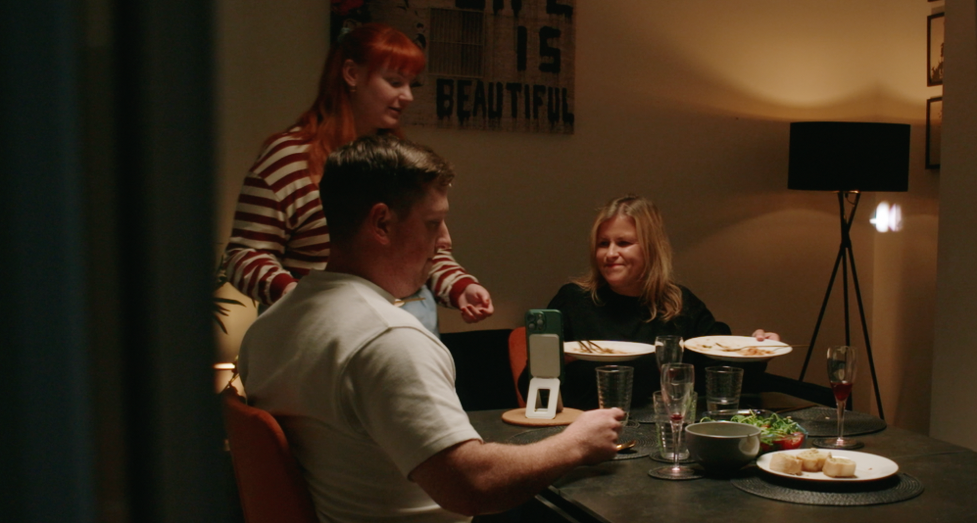 Three people at a dinner table with food. One person is looking at the phone.