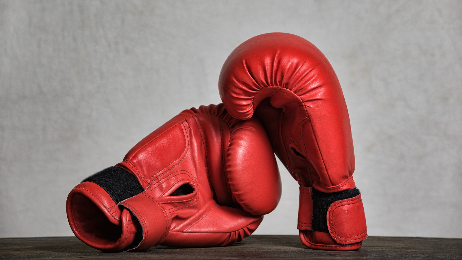 A pair of red boxing gloves are sitting on a wooden table.