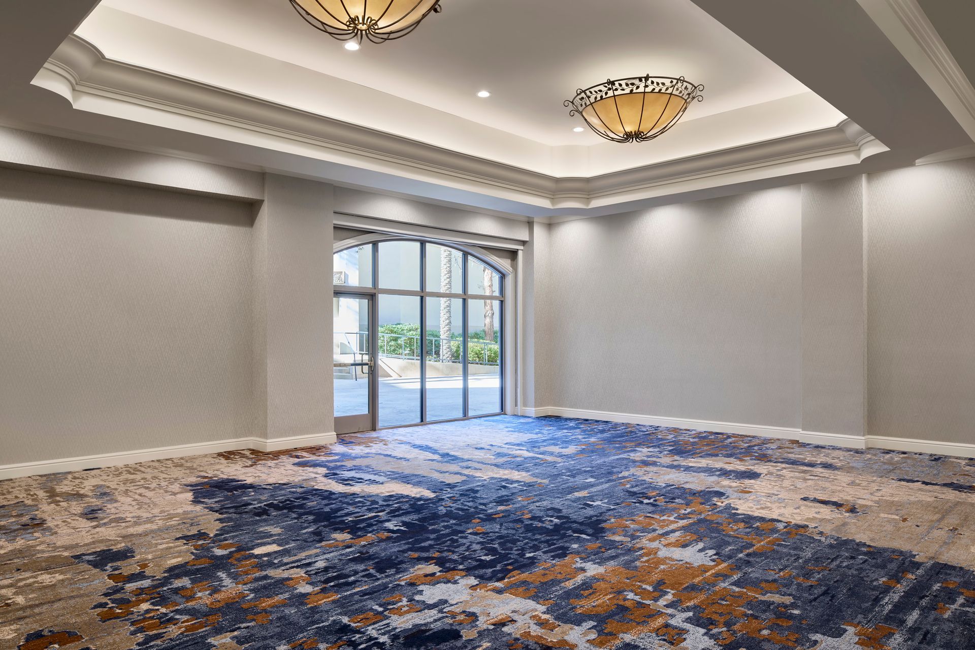 An empty room with an ornate ceiling, patterned carpet, and a glass door leading outside.