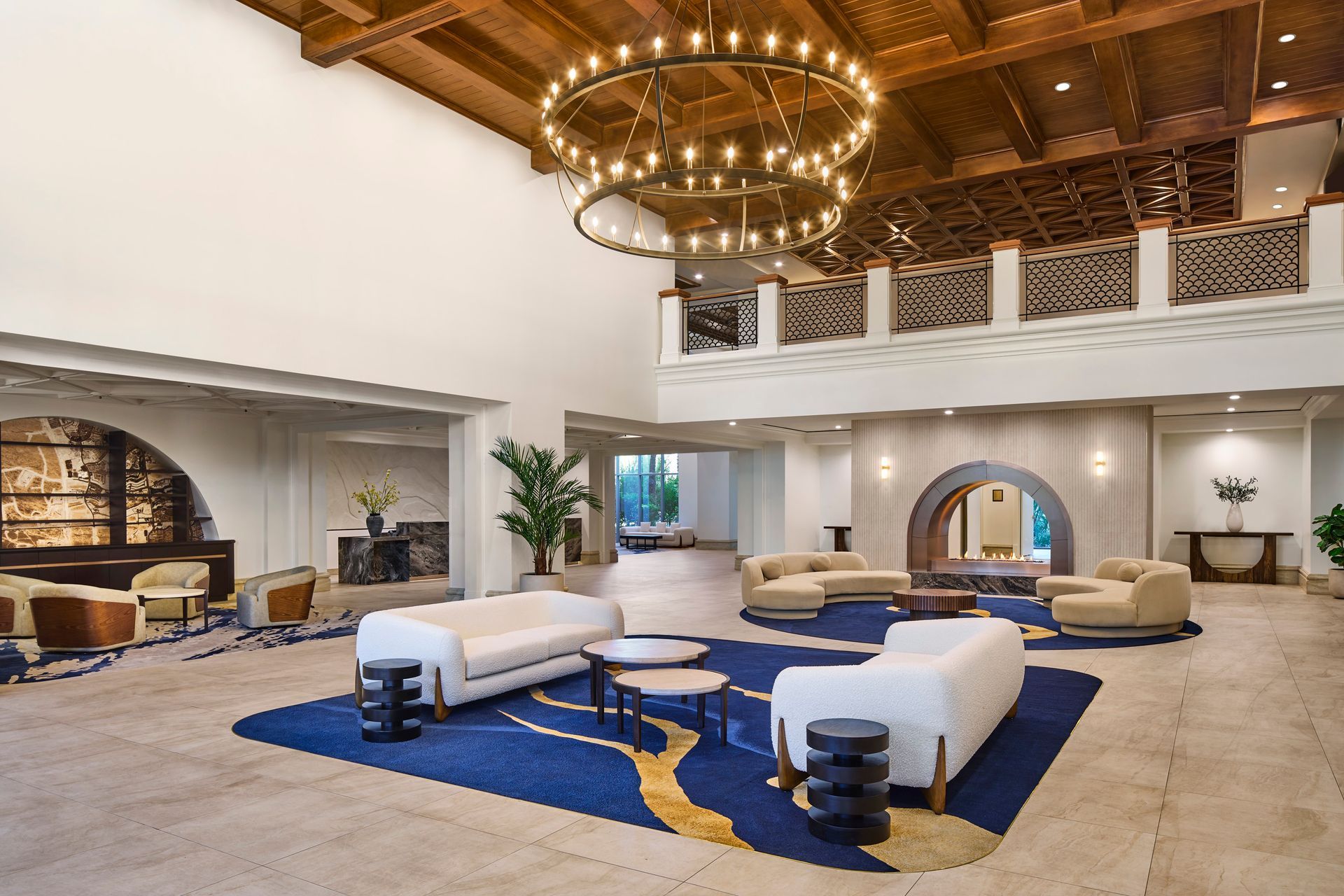 A grand lobby with white sofas on a blue patterned rug, a large chandelier, and wood accents.