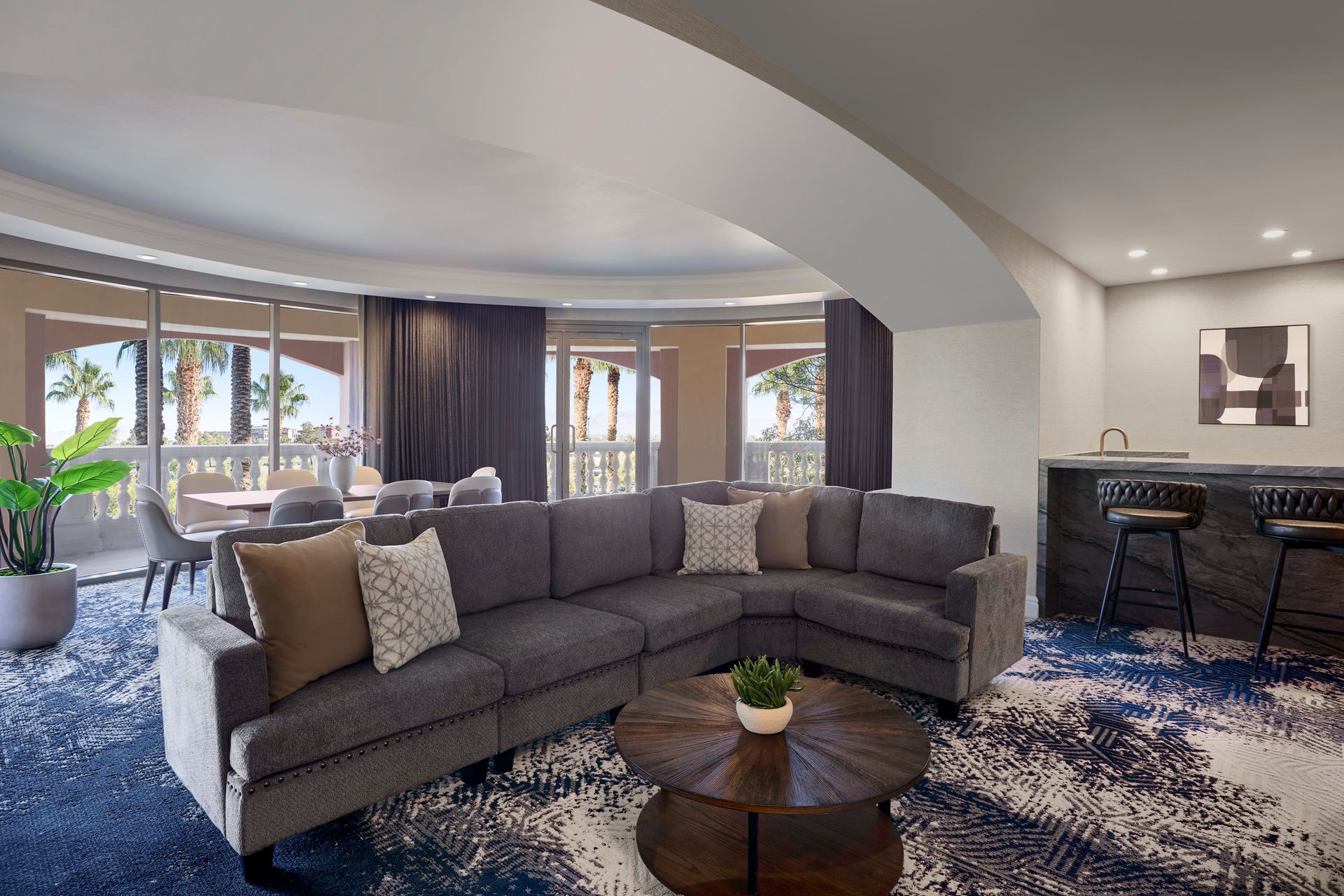 A modern living room with a sectional sofa, round coffee table, and bar area, overlooking a balcony and ocean view.