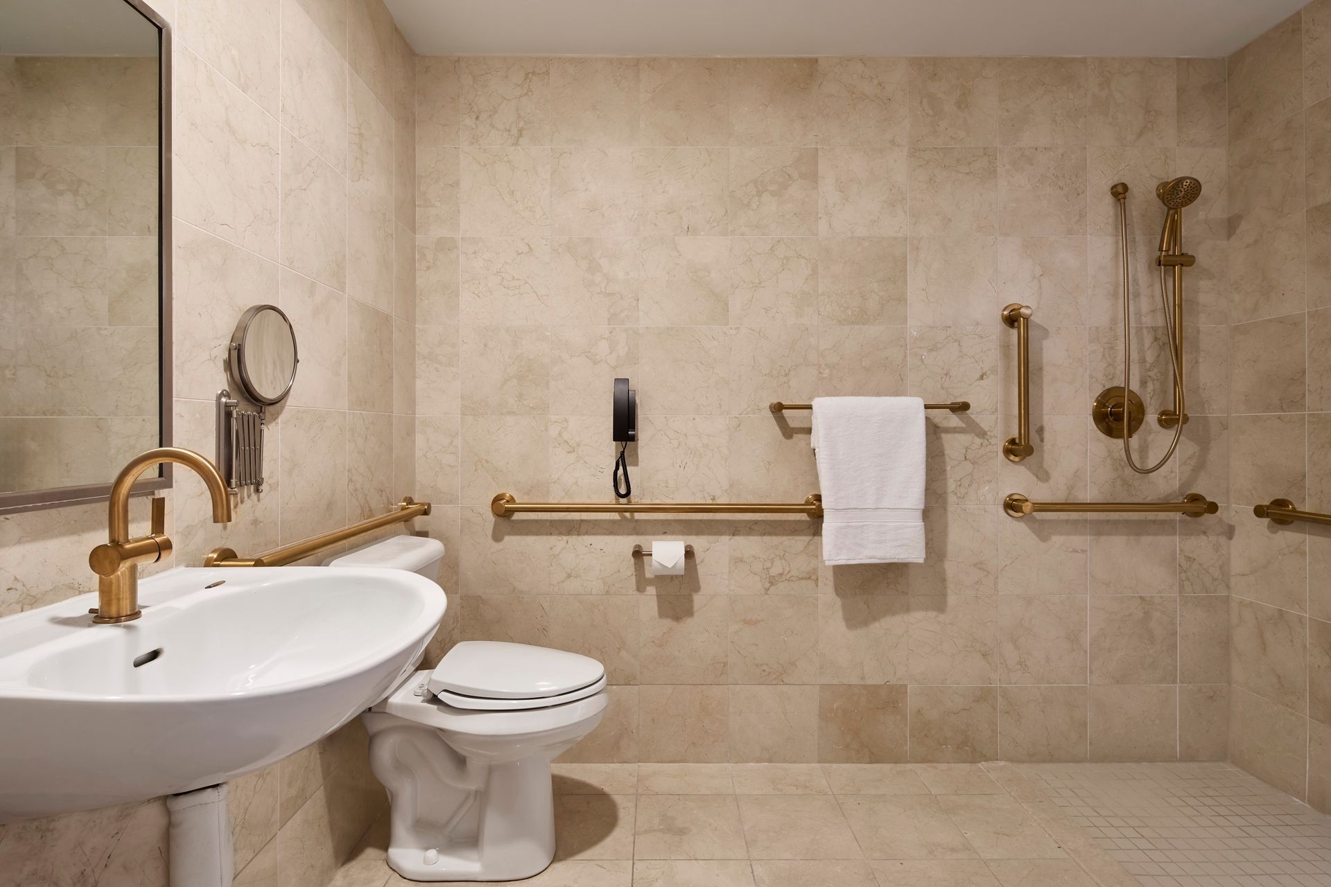 Accessible bathroom with beige tiles, gold fixtures, and grab bars. Includes a sink, toilet, shower, and towel rack.