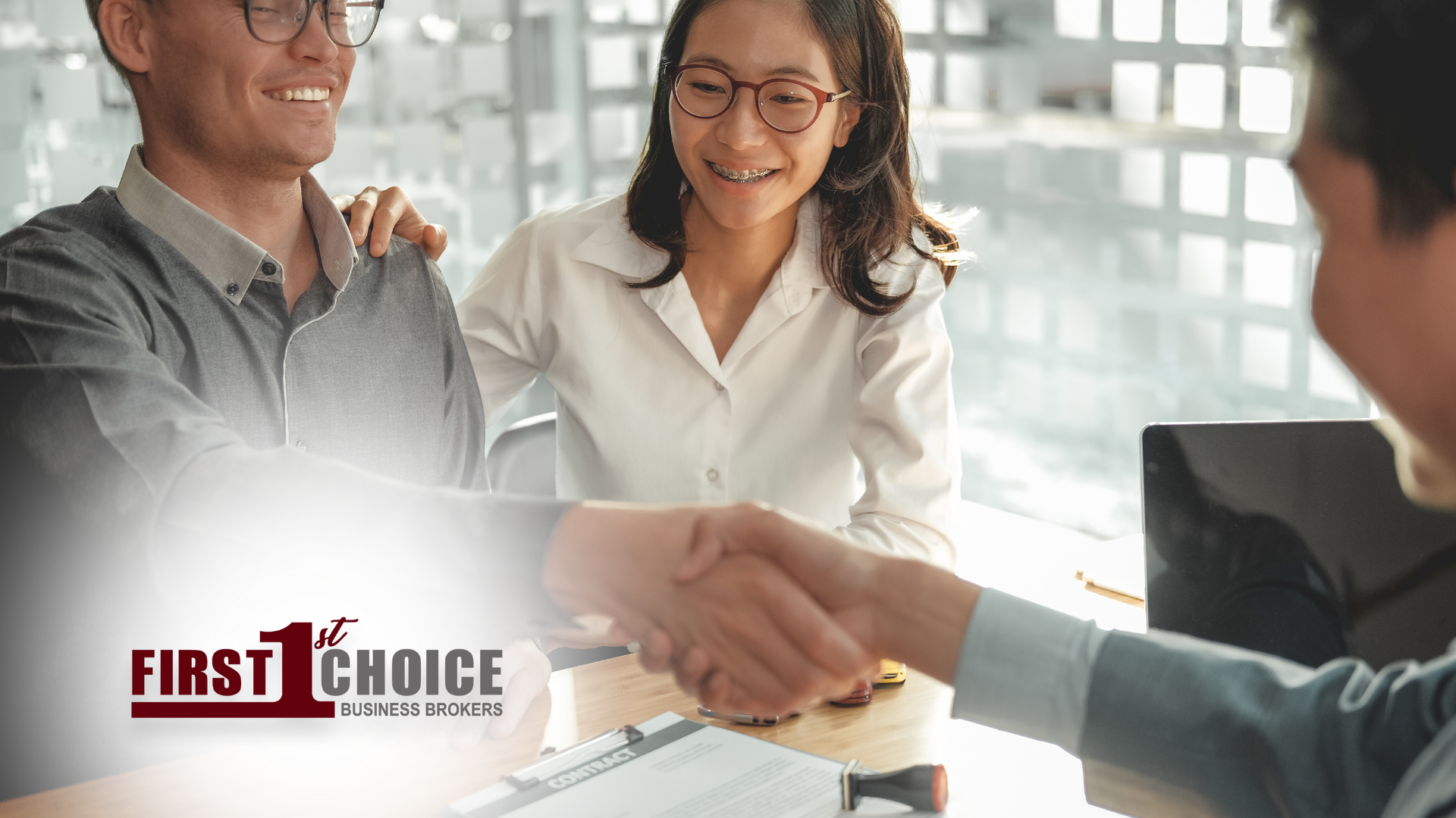 A man and a woman are shaking hands while sitting at a table.