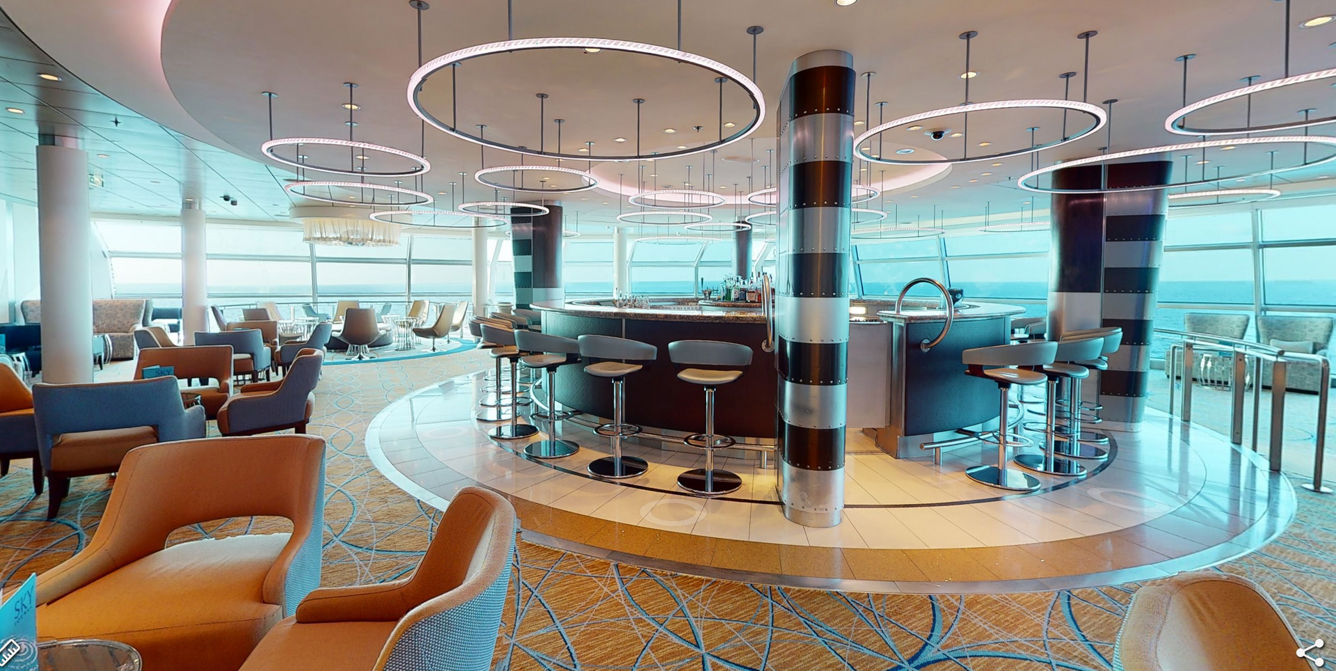 Interior of a modern bar on a cruise ship, with a circular bar, seating, and ocean views.