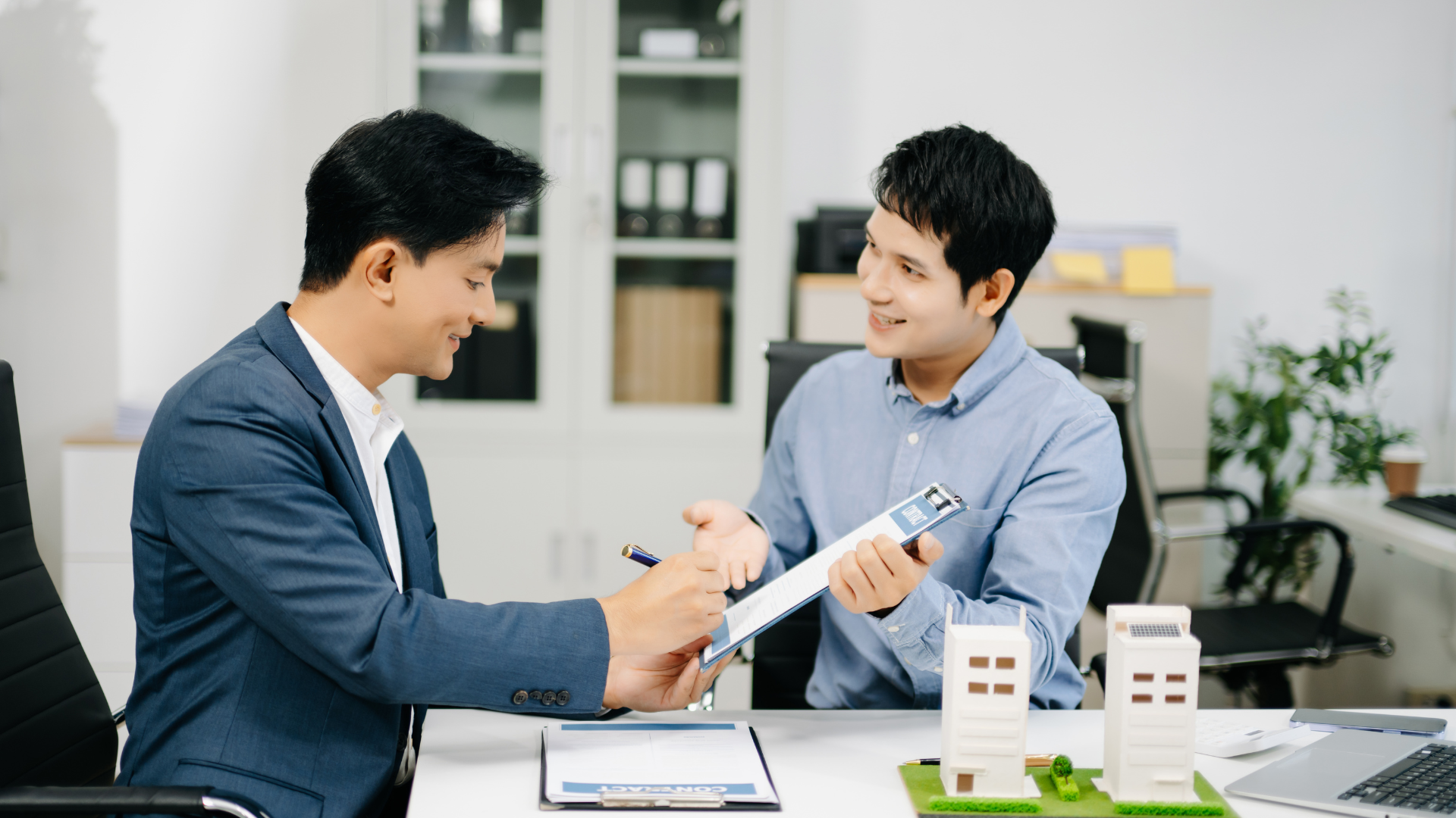 Two coworkers in a meeting reviewing documents across a desk in a bright office