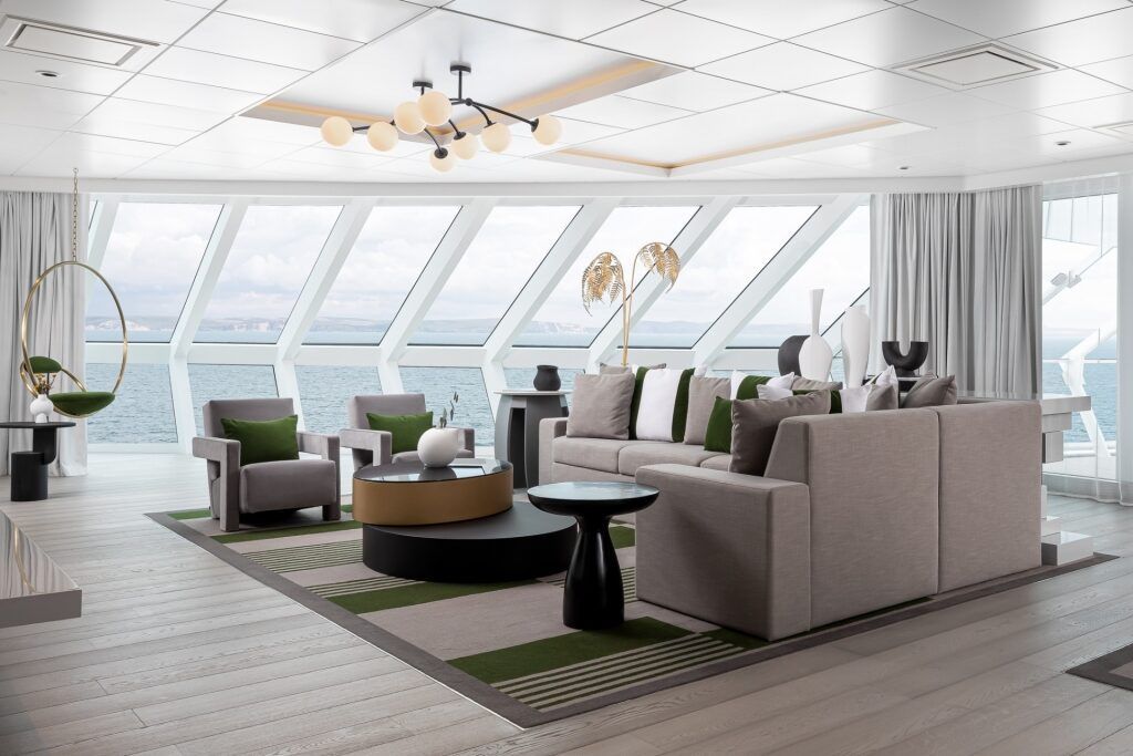 A modern living room with large windows overlooking a cityscape. Features a neutral color scheme, with a sectional sofa, armchairs, and a circular rug.