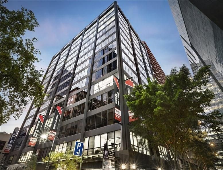 Modern office building with glass facade, flags, and parking sign on a city street.