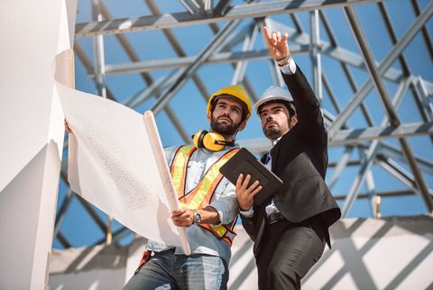 Two construction workers reviewing blueprints on a building site.