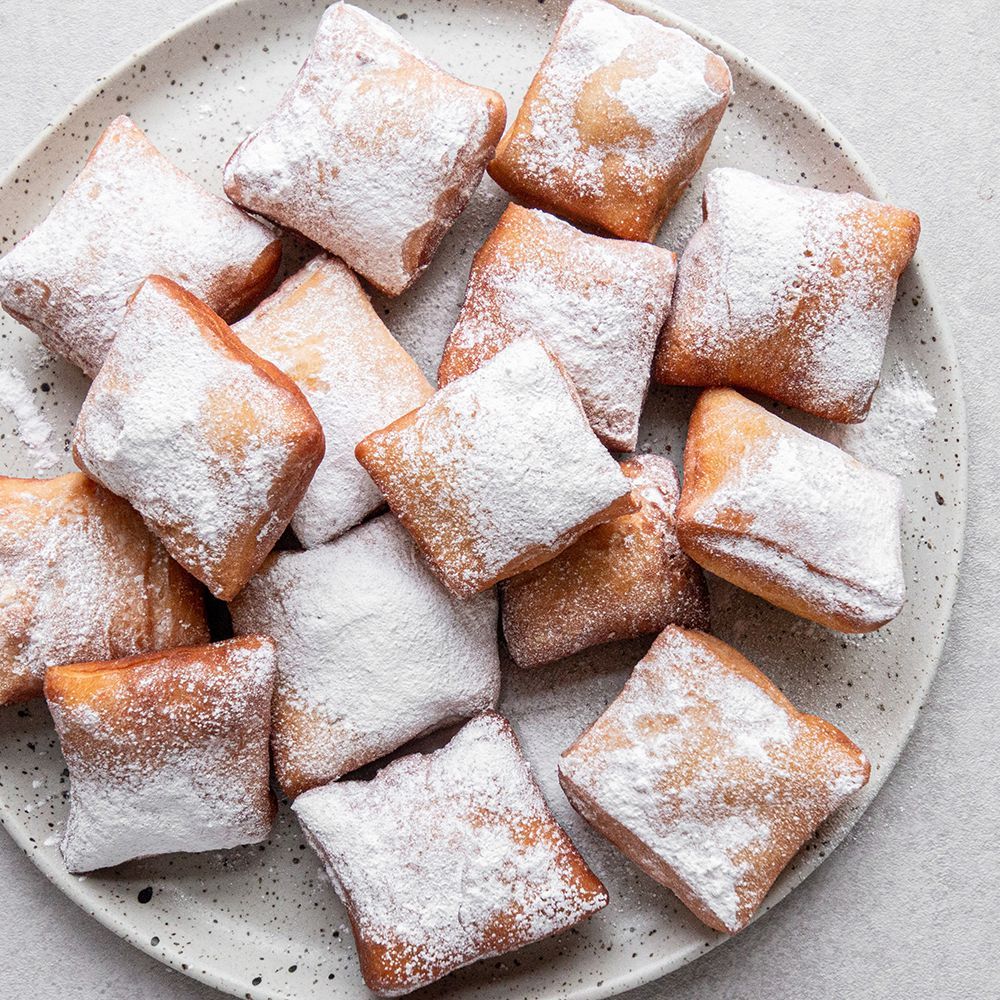 A plate of doughnuts covered in powdered sugar on a table.