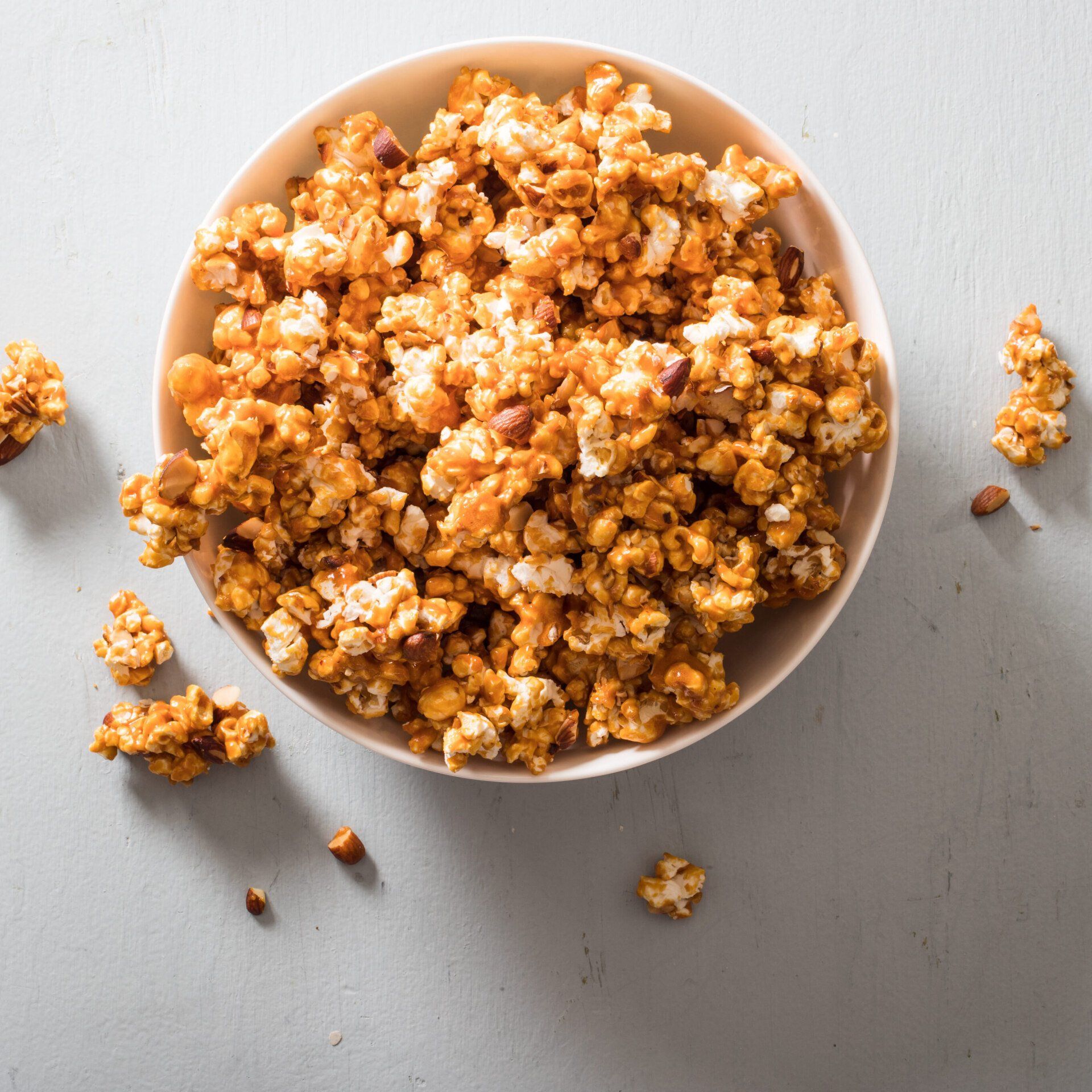 A bowl of caramel popcorn with nuts on a table