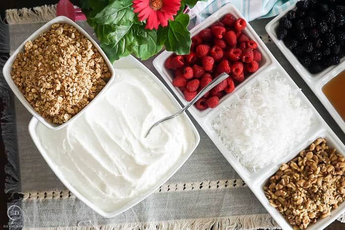 A table topped with bowls of yogurt , raspberries , coconut , and granola.