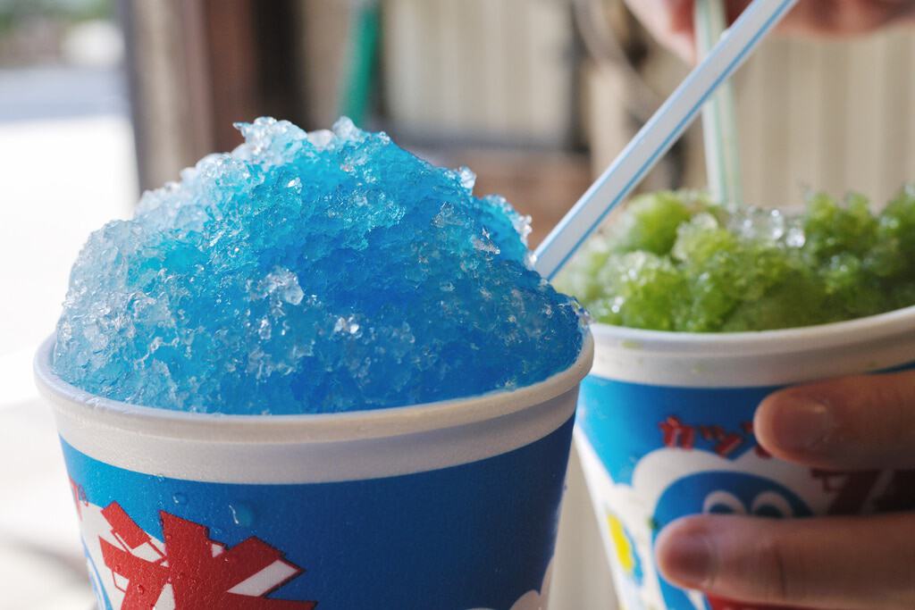 A person is holding two cups of shaved ice with straws.