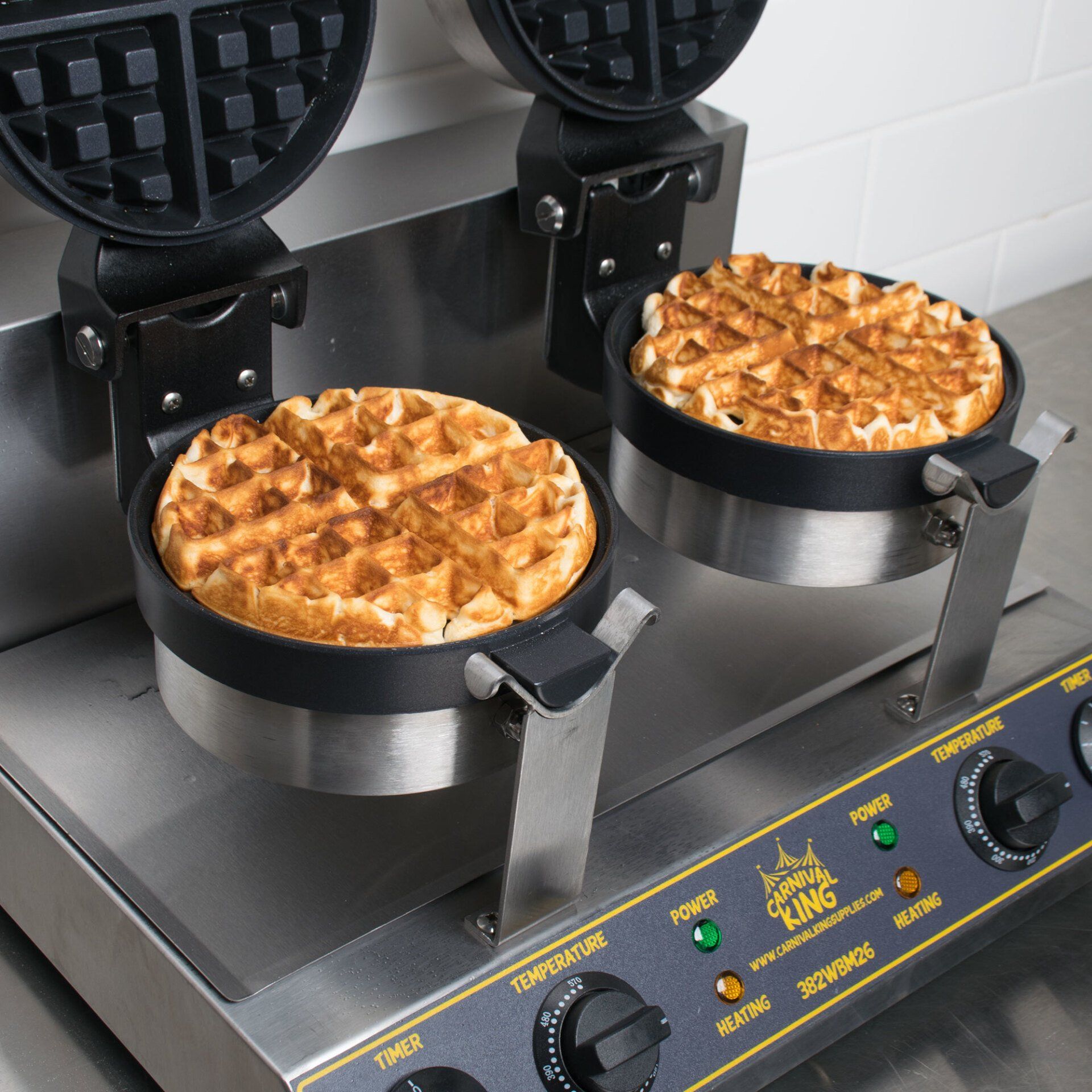 Two waffles are cooking on a waffle maker that says king