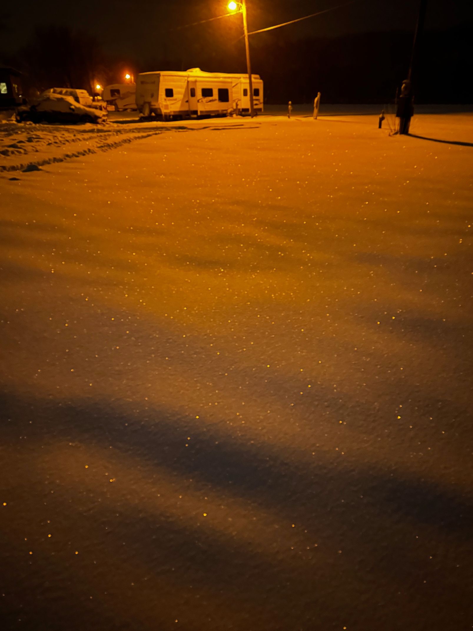 Snow-covered road at night with parked vehicles under orange streetlights