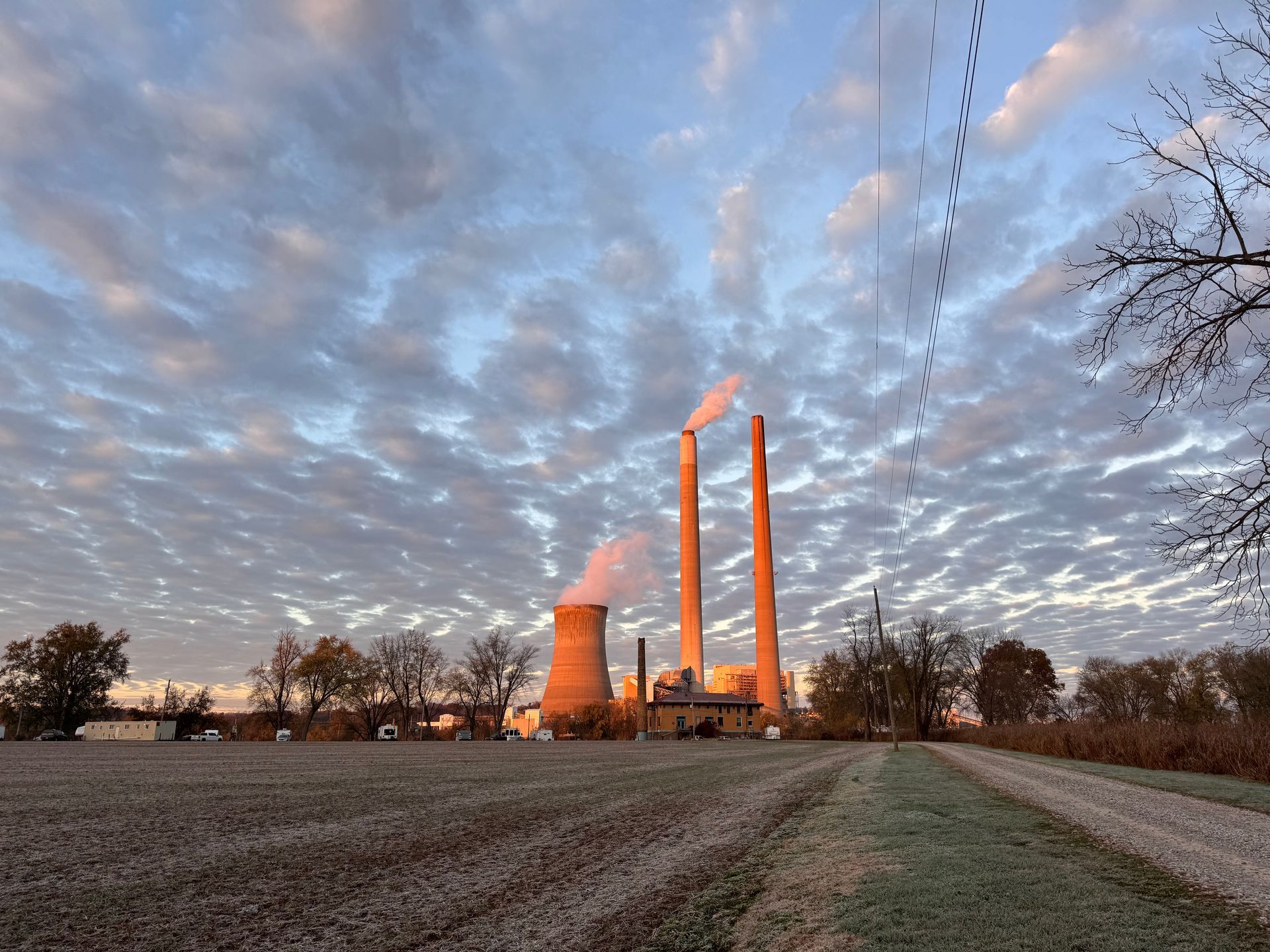 Industrial plant with two tall smokestacks at sunset under a cloudy sky, beside a frosty field and path