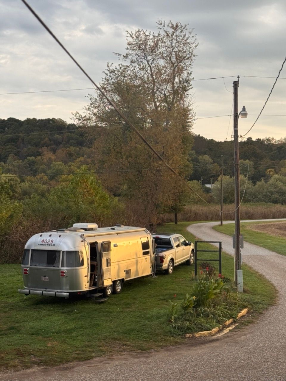 Silver camper trailer and pickup parked on grass beside a winding road at dusk