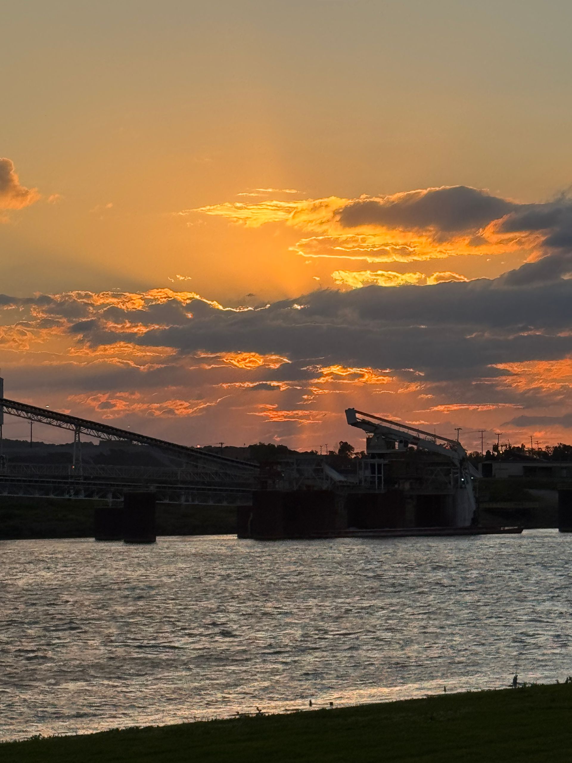 Sunset over a river with silhouetted industrial cranes and glowing orange clouds