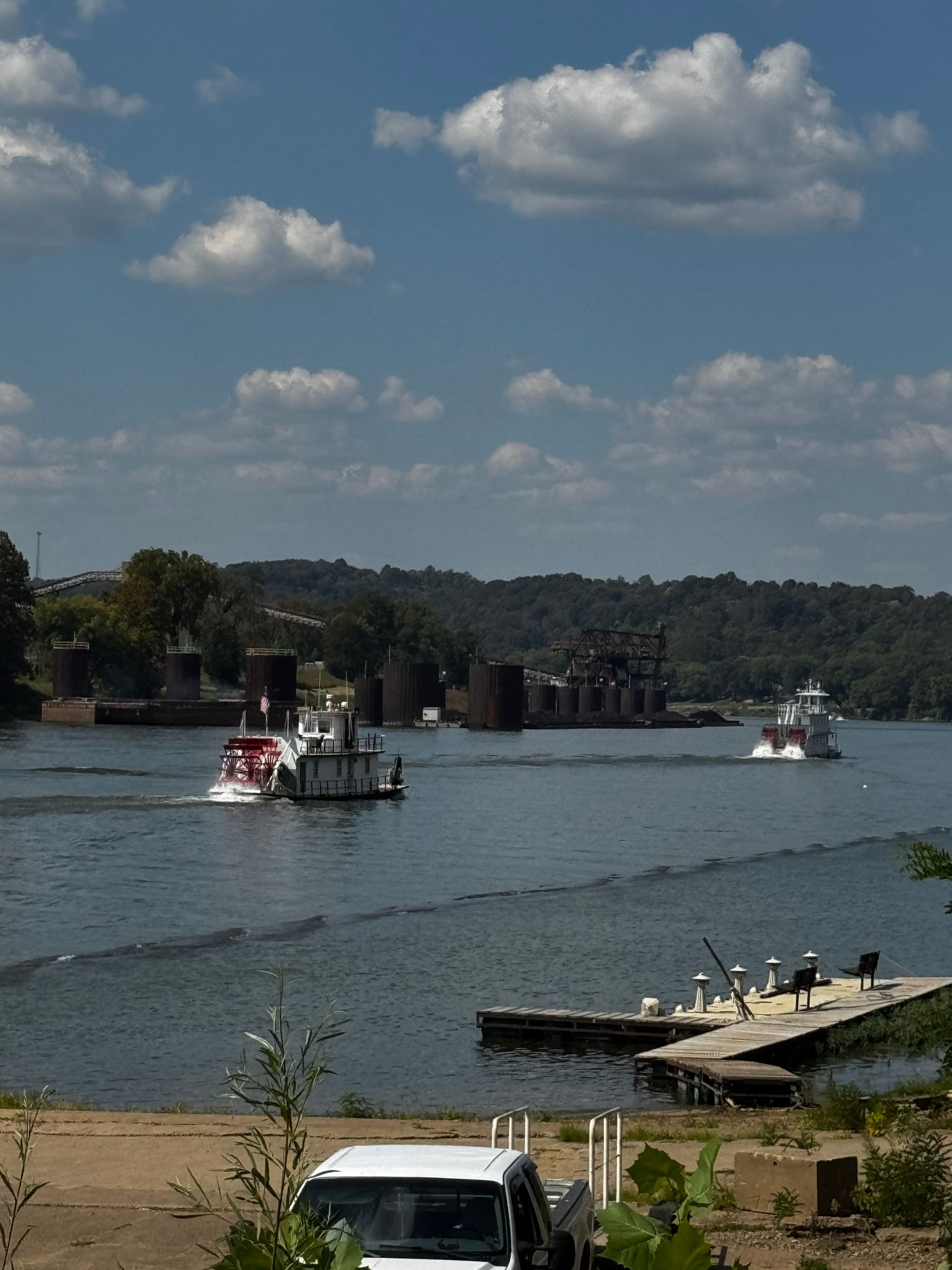 Boats on a river near a sandy shore and dock under a partly cloudy sky