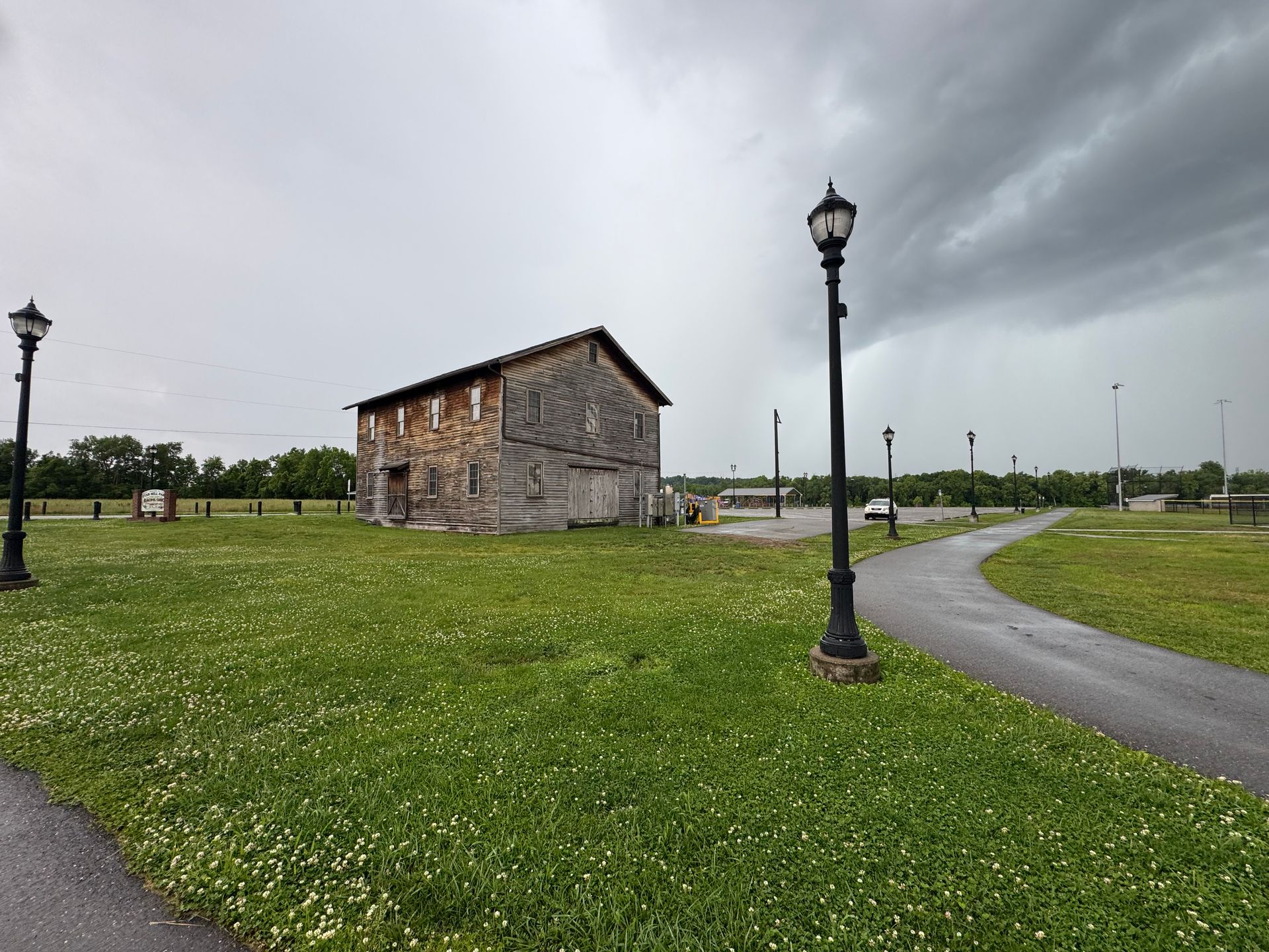 Small stone building in a grassy park under cloudy skies, with a curving path and lampposts.