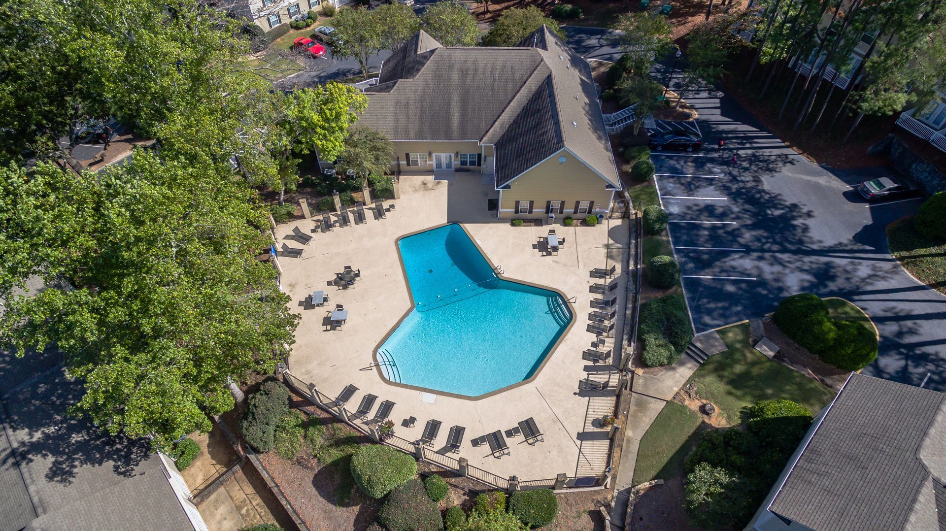 Aerial view of a swimming pool surrounded by lounge chairs and a building at a community complex.
