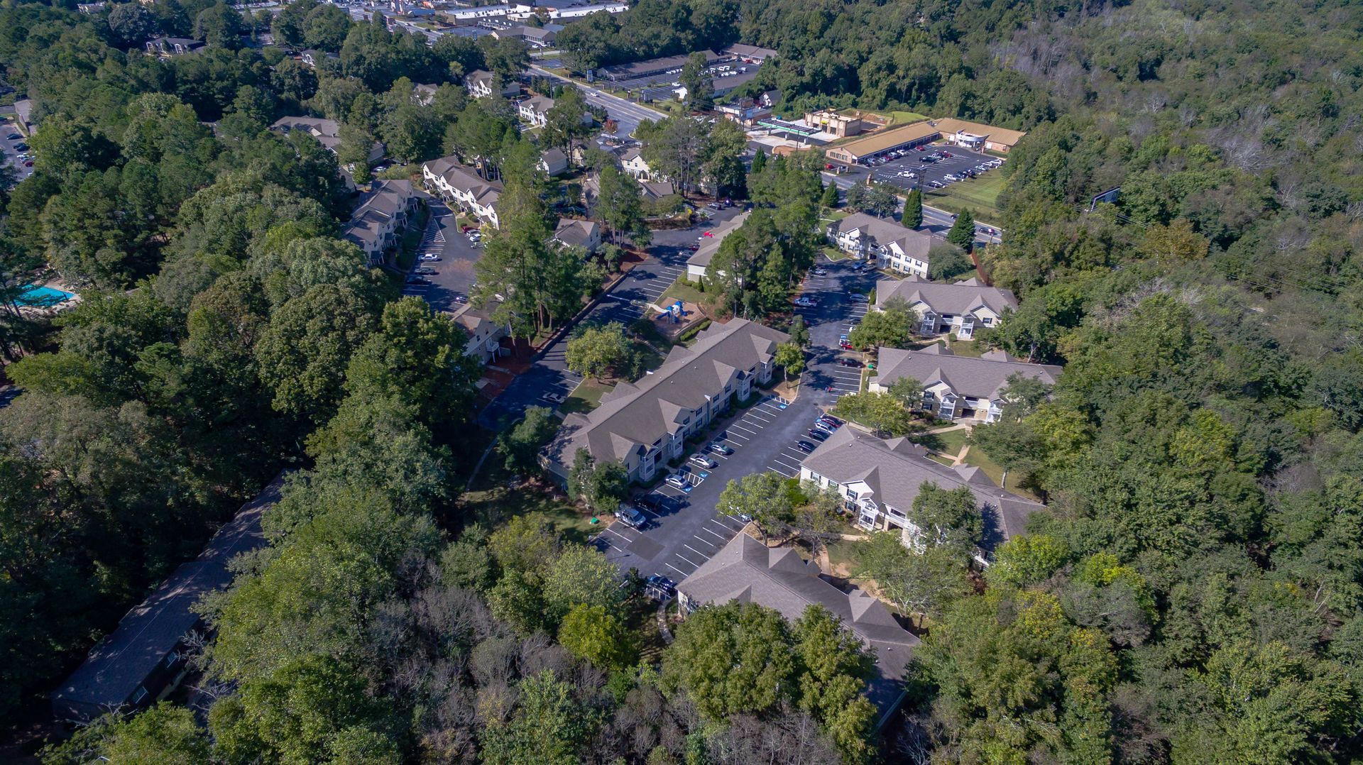 Aerial view of a multi-building apartment complex nestled within a dense forest, featuring parking lots and tree cover.
